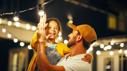 A father and daughter high-fiving after installing a new light bulb outside.