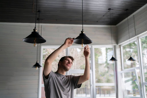 A man changing a light bulb inside of a house.